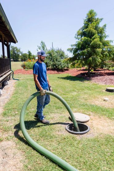 Man pumping septic tank with a green hose on a sunny day.