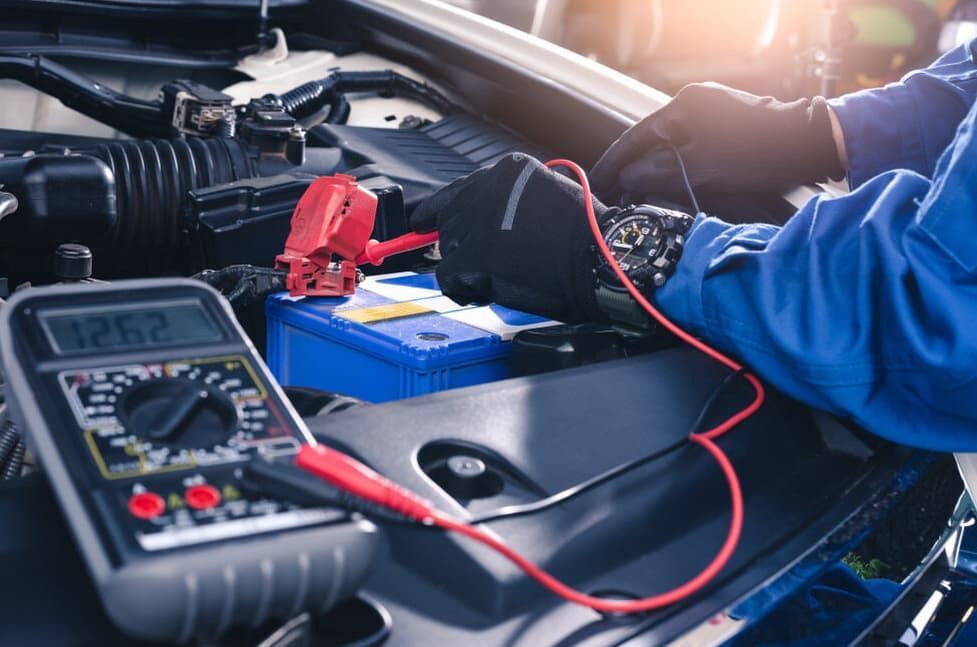 Mechanic Testing A Car Battery With A Multimeter In An Engine Bay — MC Automotive Service & Repairs in Maitland, NSW