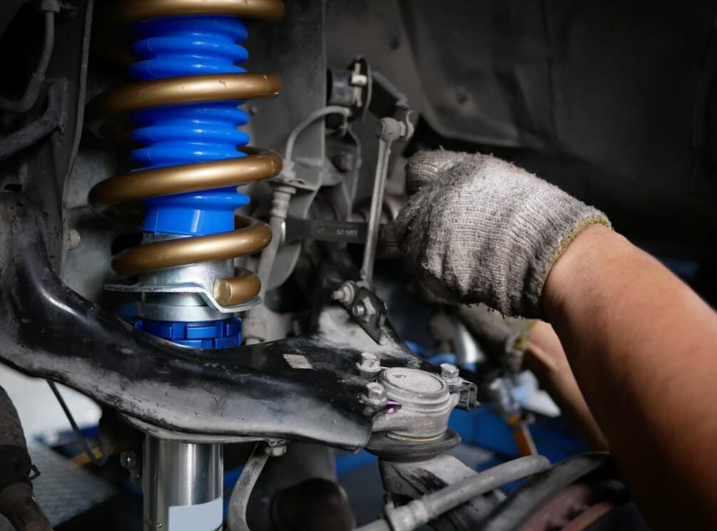 Gloved Hand Using A Wrench On Car Suspension — MC Automotive Service & Repairs in Maitland, NSW