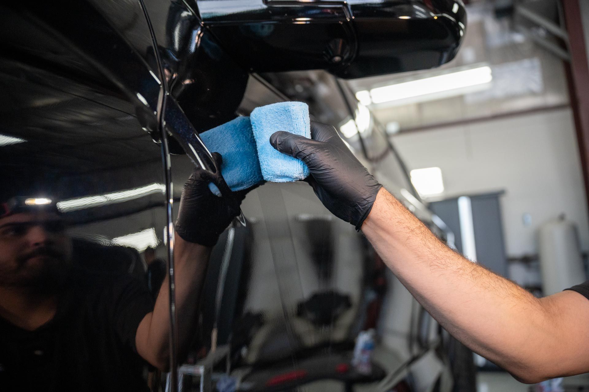 Person in black gloves applying a blue microfiber cloth to the side of a black vehicle.