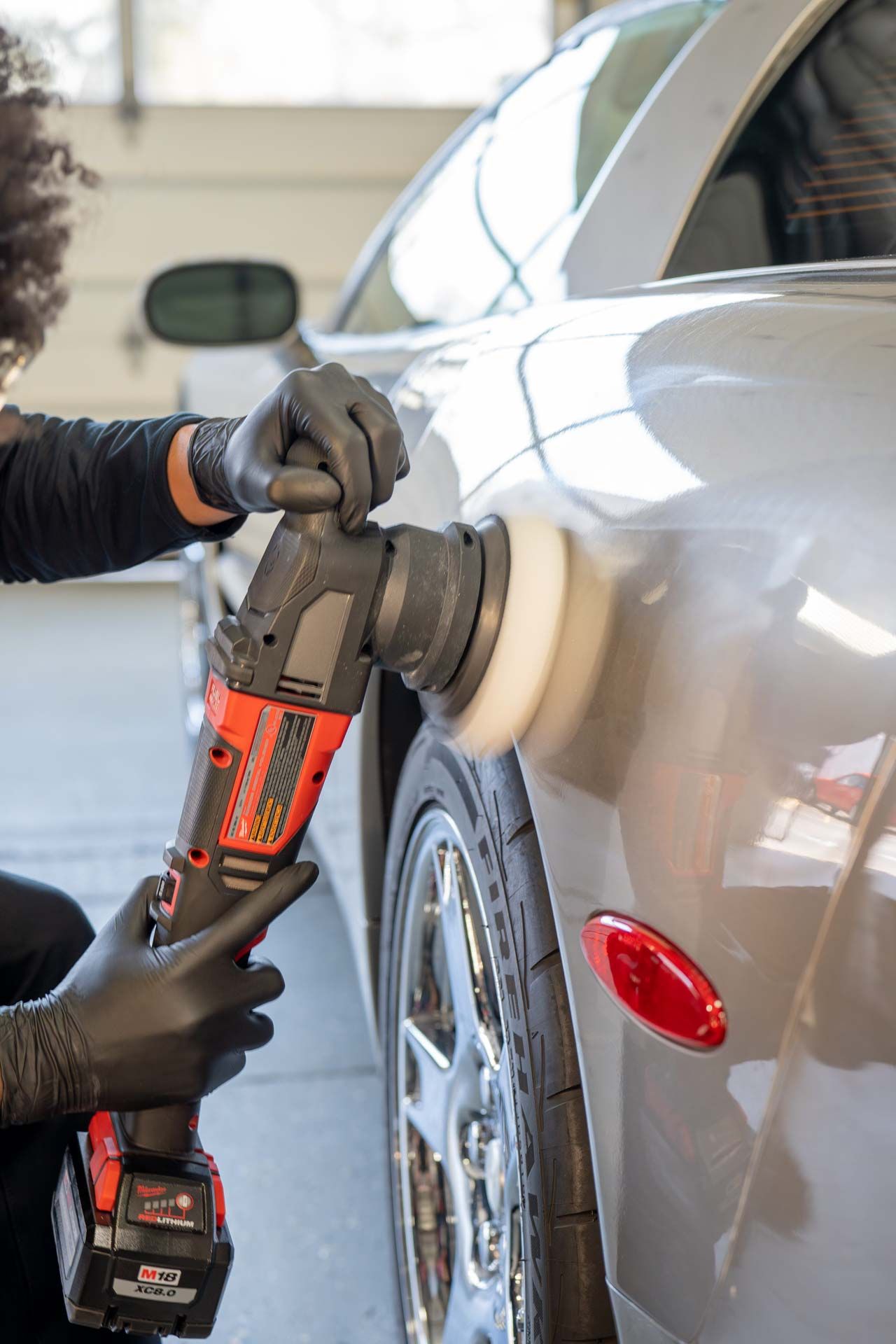 Person polishing a silver car with a power buffer in a garage.
