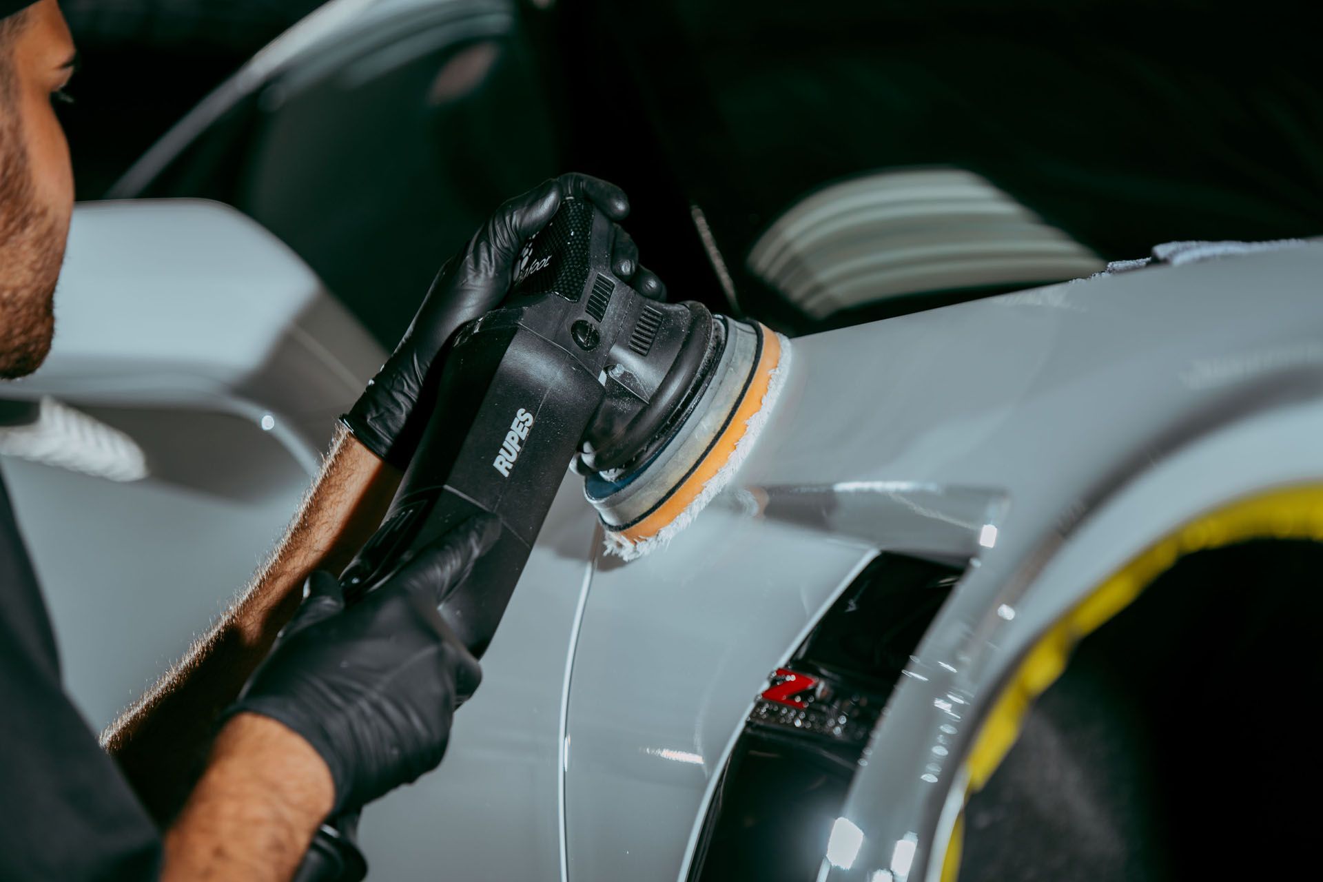 Person polishing a white car with a power buffer; close-up shows detail on the fender.