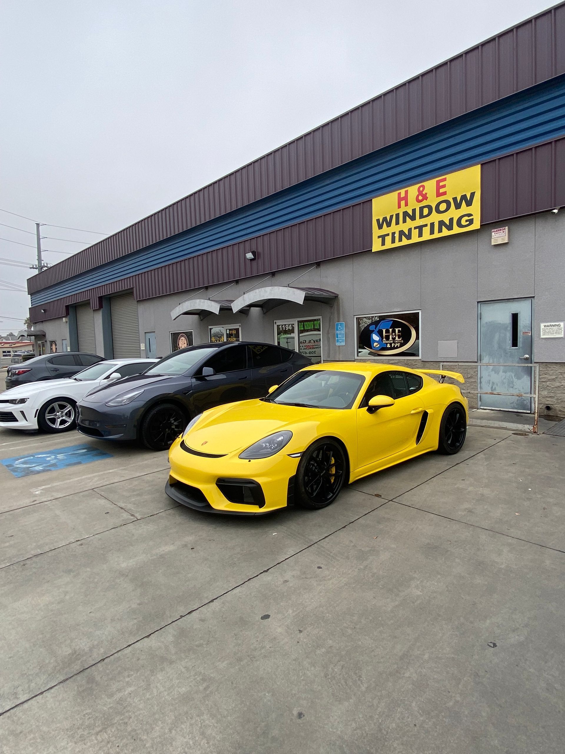 Yellow sports car parked in front of a window tinting shop with other cars.