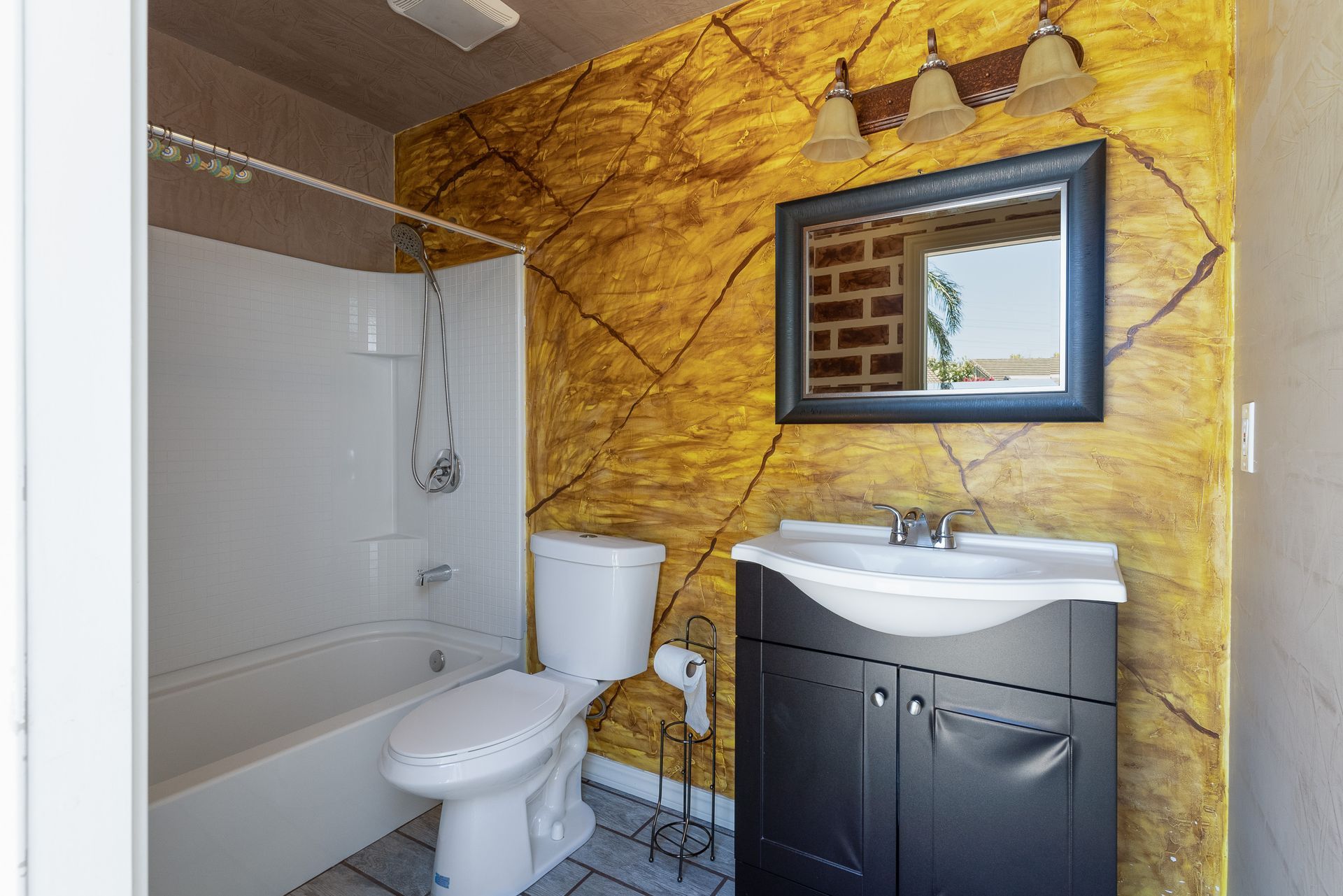 Bathroom with white tub, toilet, black vanity, and gold textured wall.