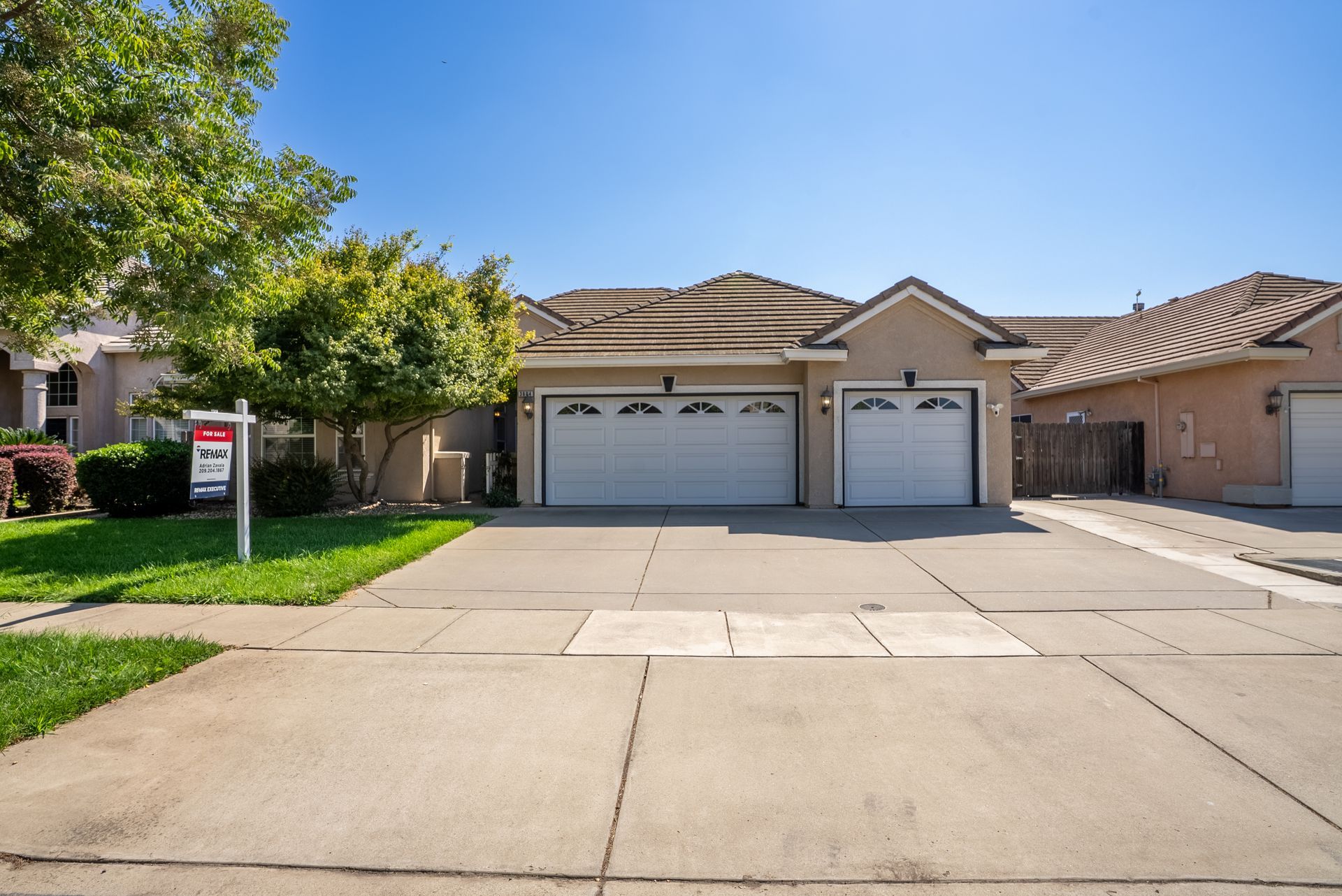 House exterior with a two-car garage, driveway, and for sale sign on a sunny day.