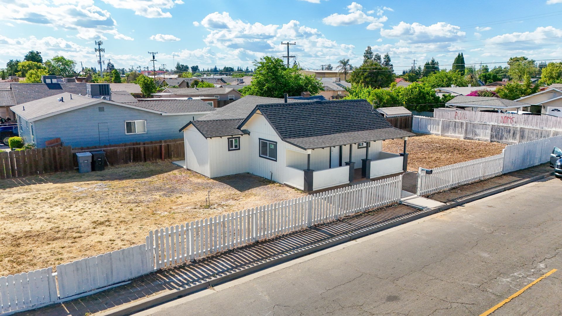 Small white house with a black roof and a picket fence on a sunny day.