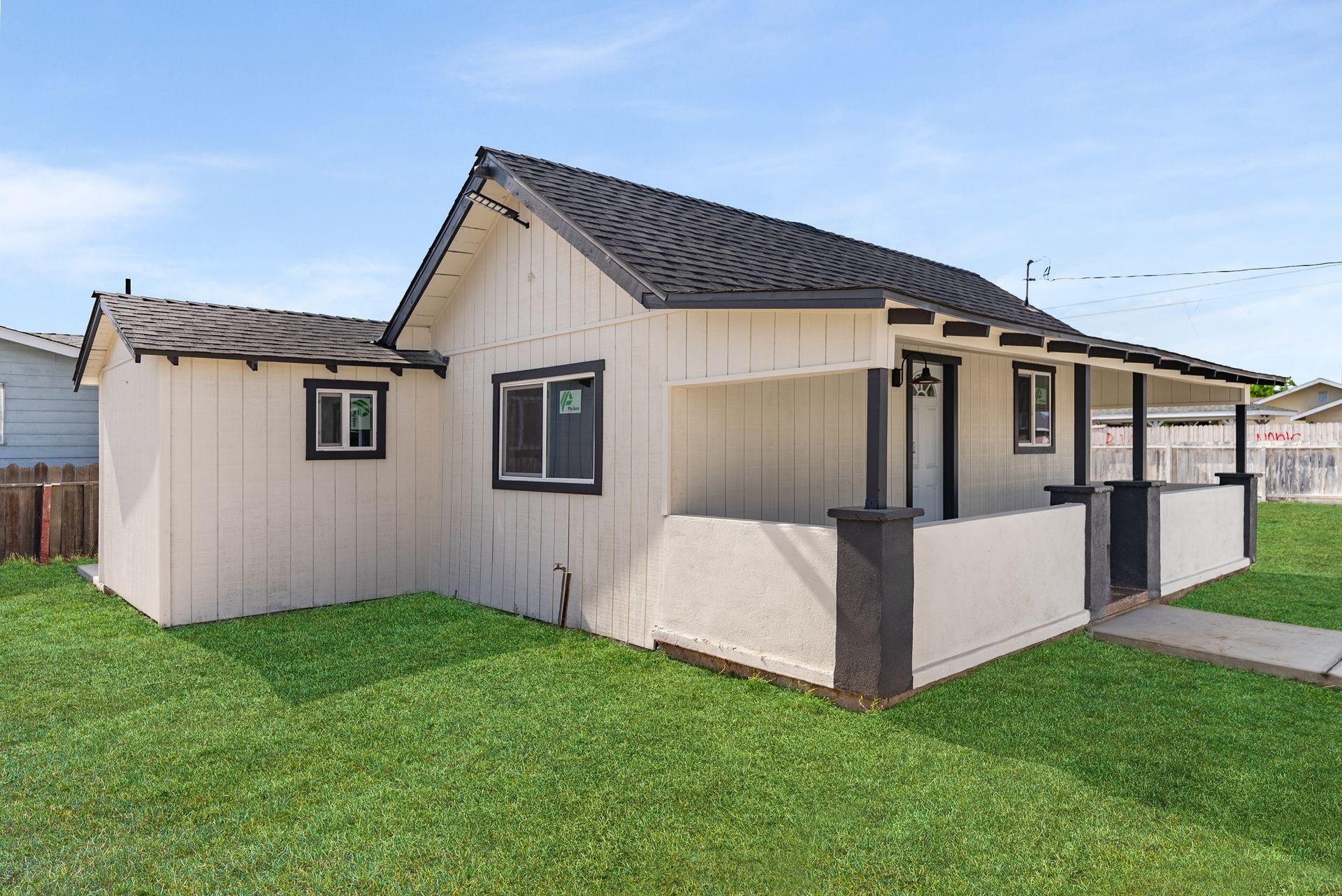 White house with black trim and roof, set on green grass under a blue sky.
