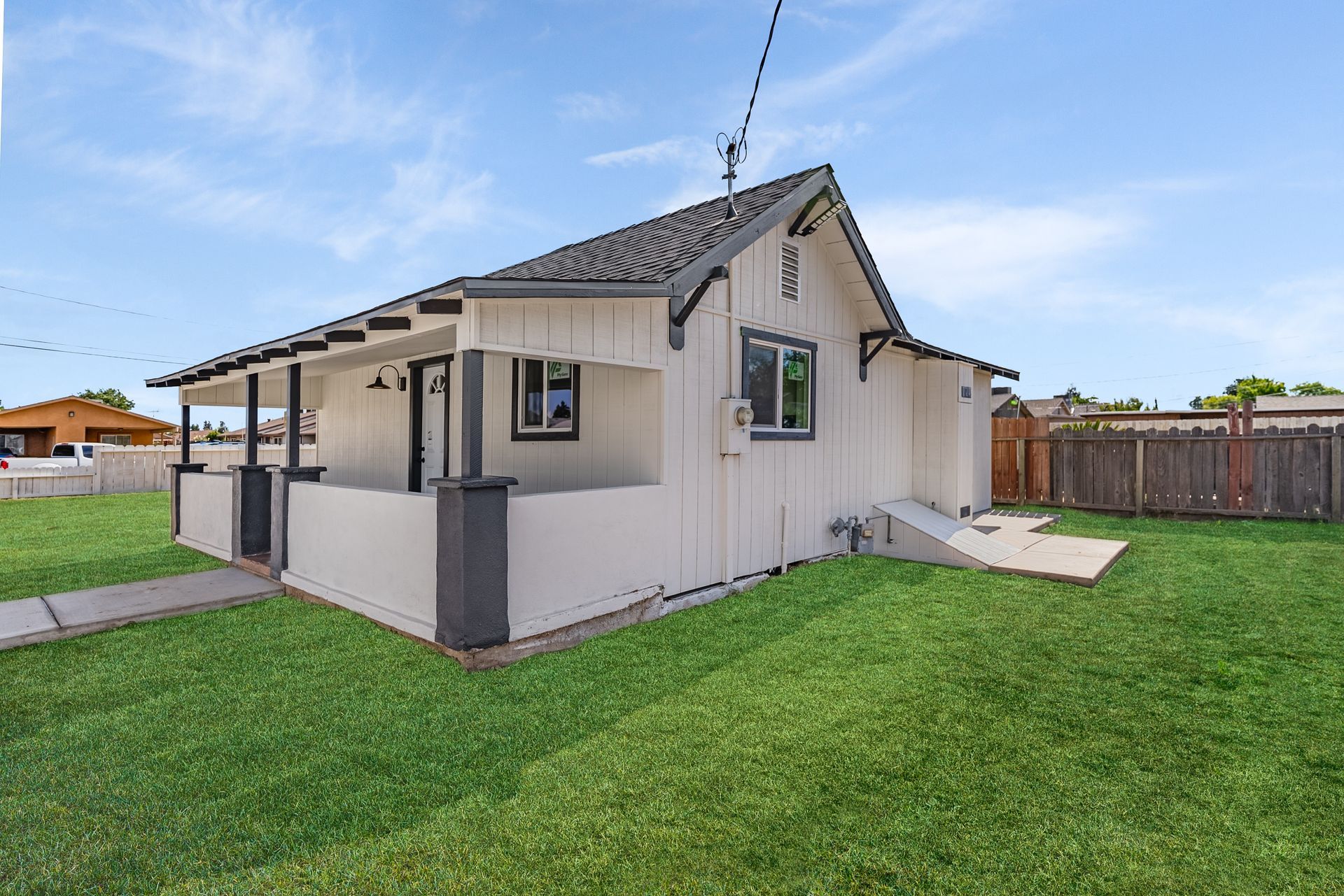 White house with black trim, front porch, and green lawn under a blue sky.