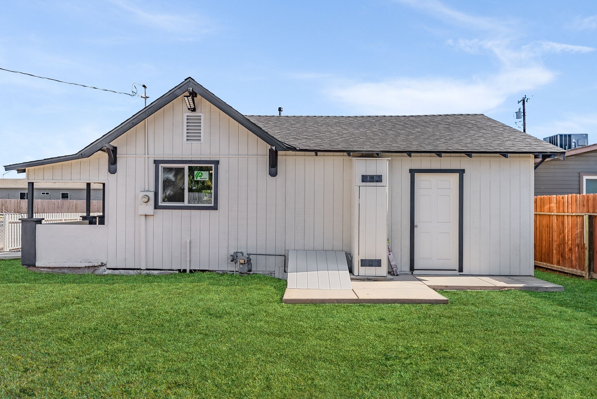 White building with a dark roof, small green lawn. Door and window visible.