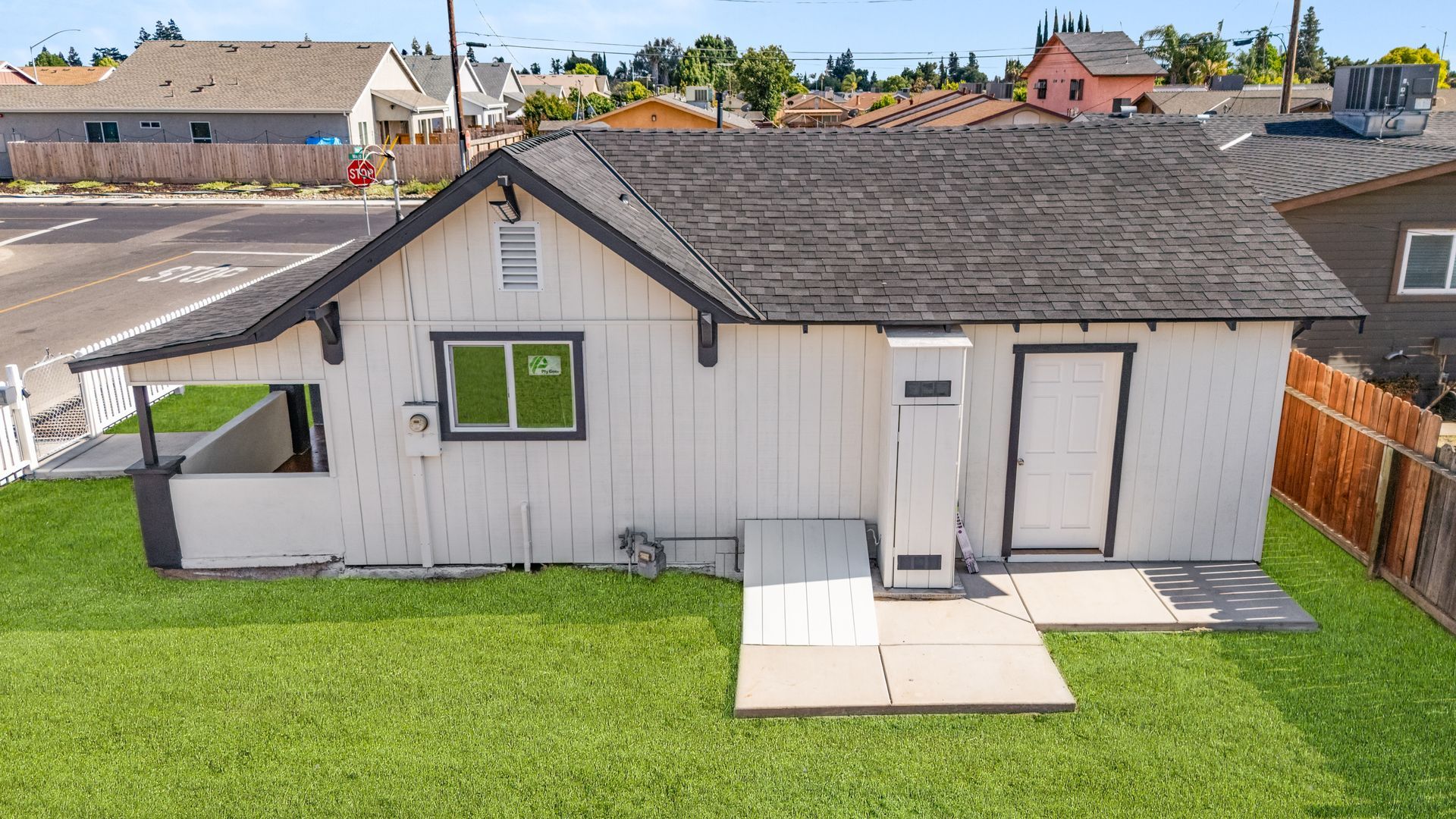 Back view of a small white house with a black roof, a small porch, and green grass.