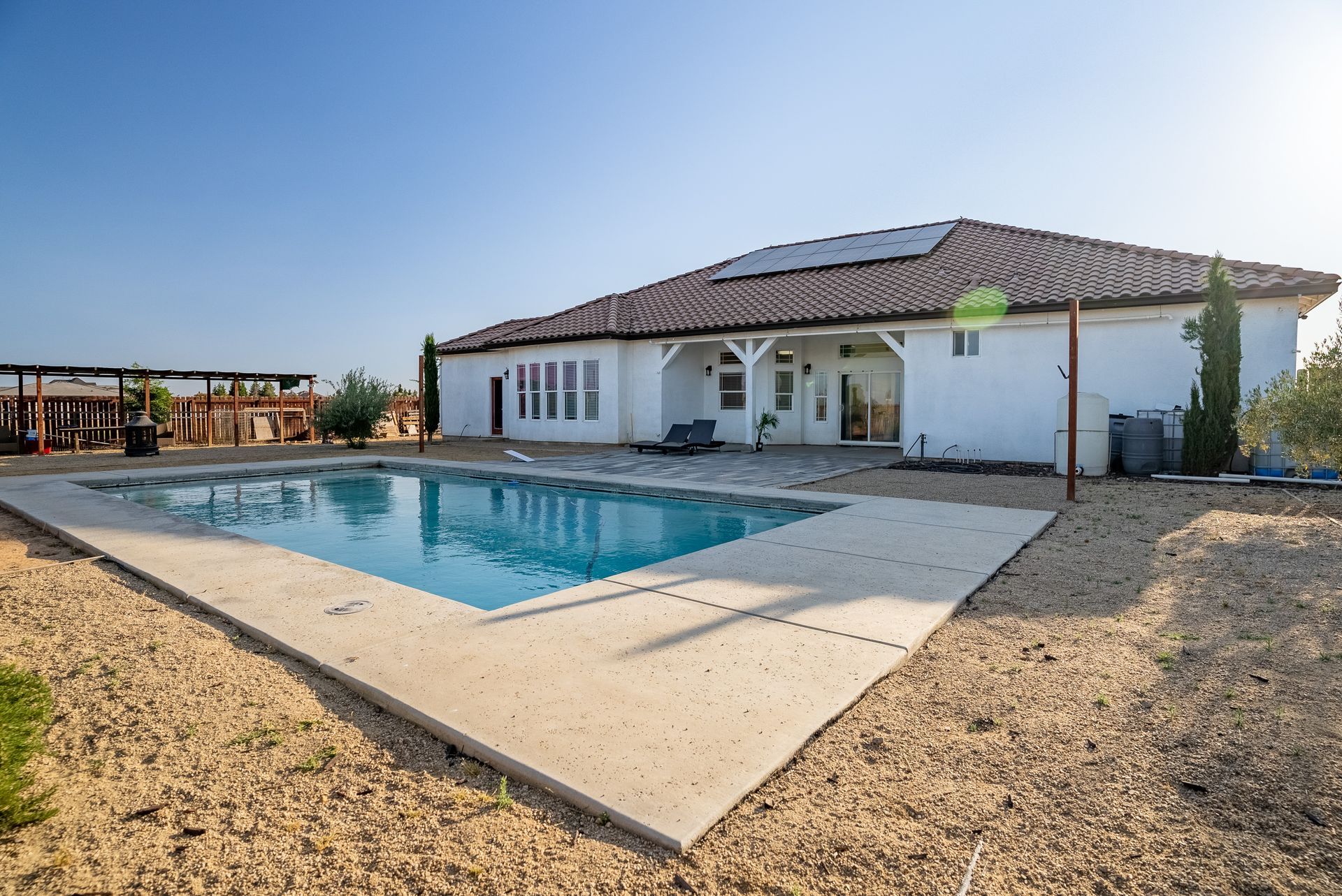 Backyard with pool and white house under a bright blue sky.