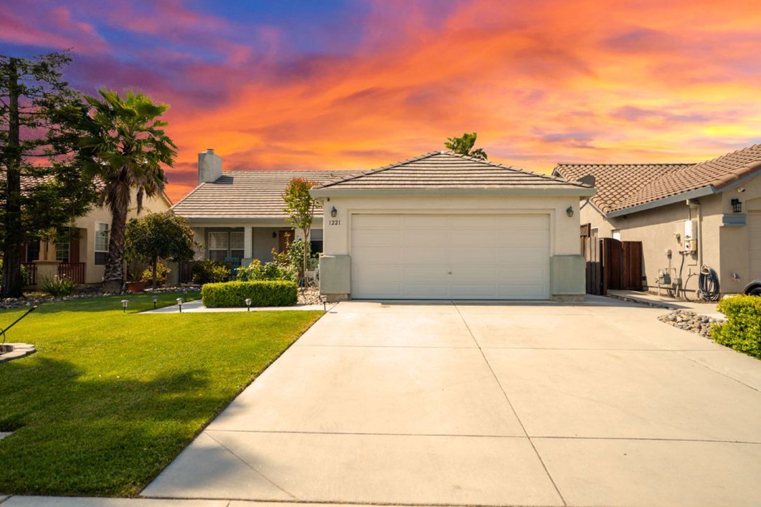 House with a two-car garage and driveway, set under a vibrant sunset sky.