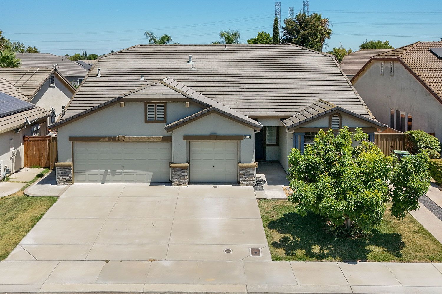 Two-story beige house with a two-car garage, green bush in front, and clear blue sky.