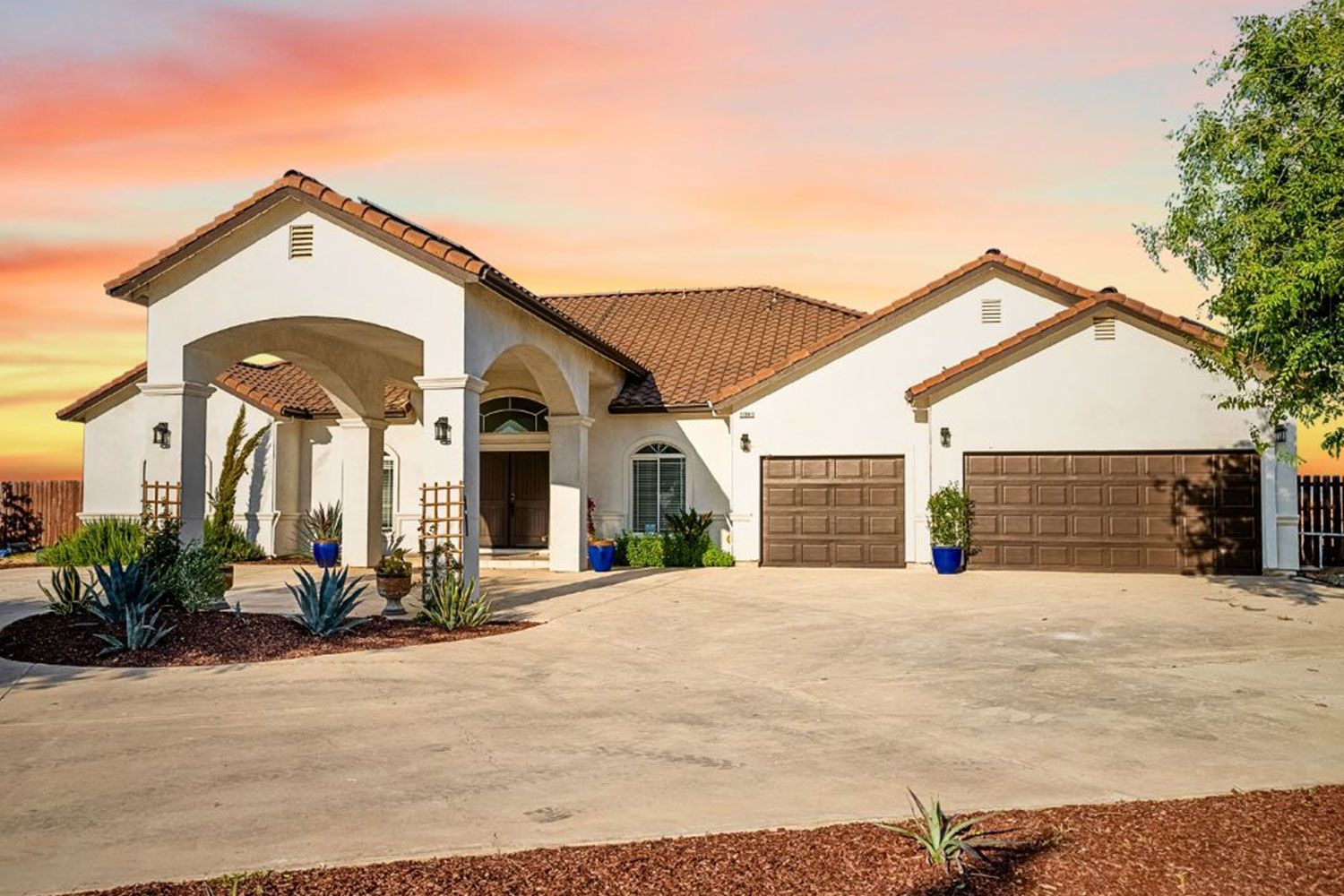 White stucco house with brown garage doors and clay tile roof at sunset.