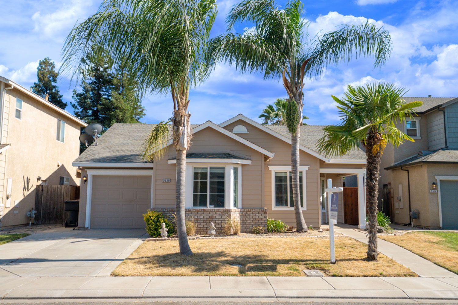 Tan house with a light-colored roof and palm trees in front.