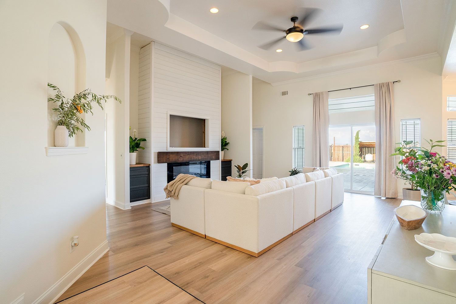 Spacious living room with a white sectional, fireplace, and large windows overlooking a yard.