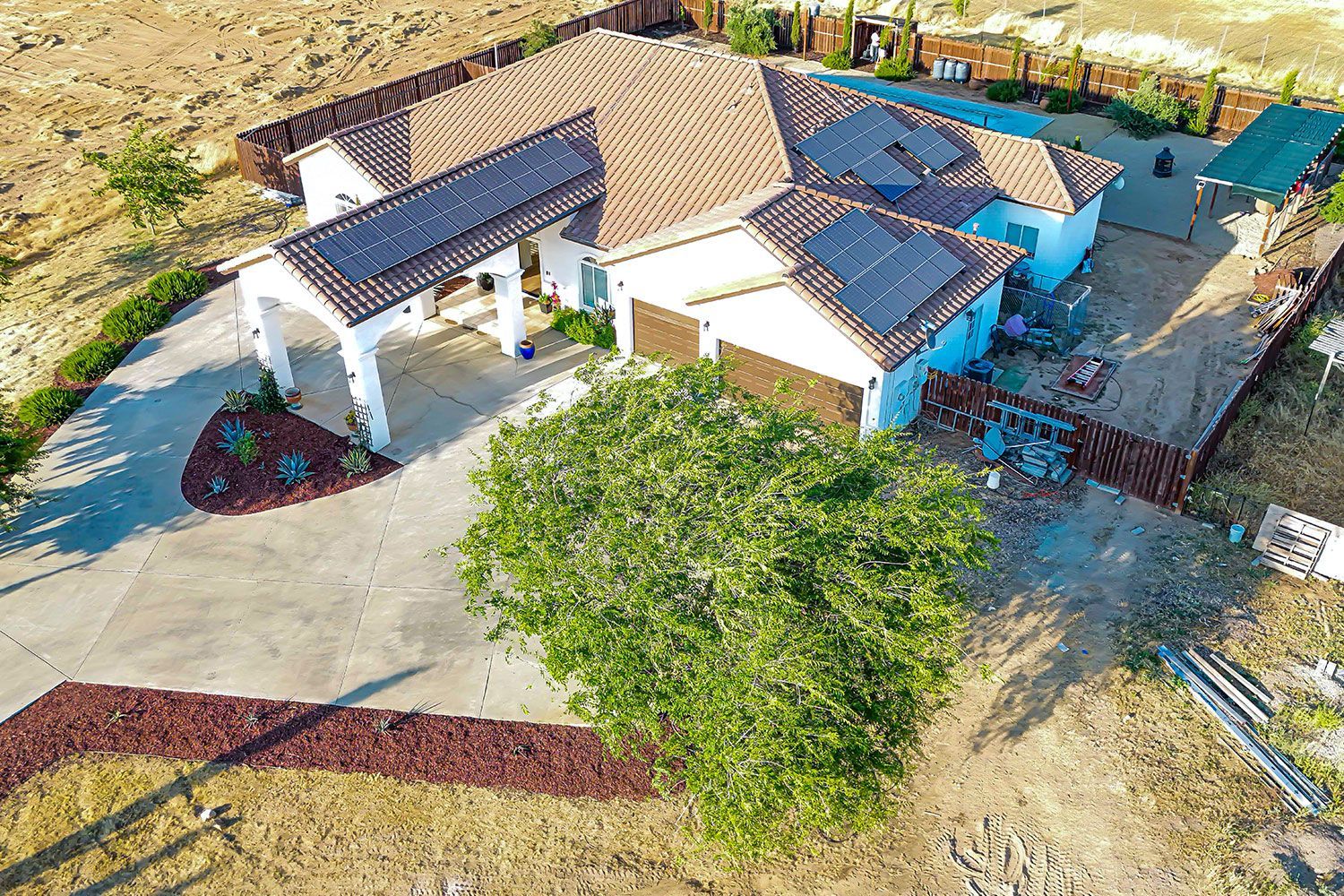 Aerial view of a house with solar panels, a driveway, and a large tree in front.