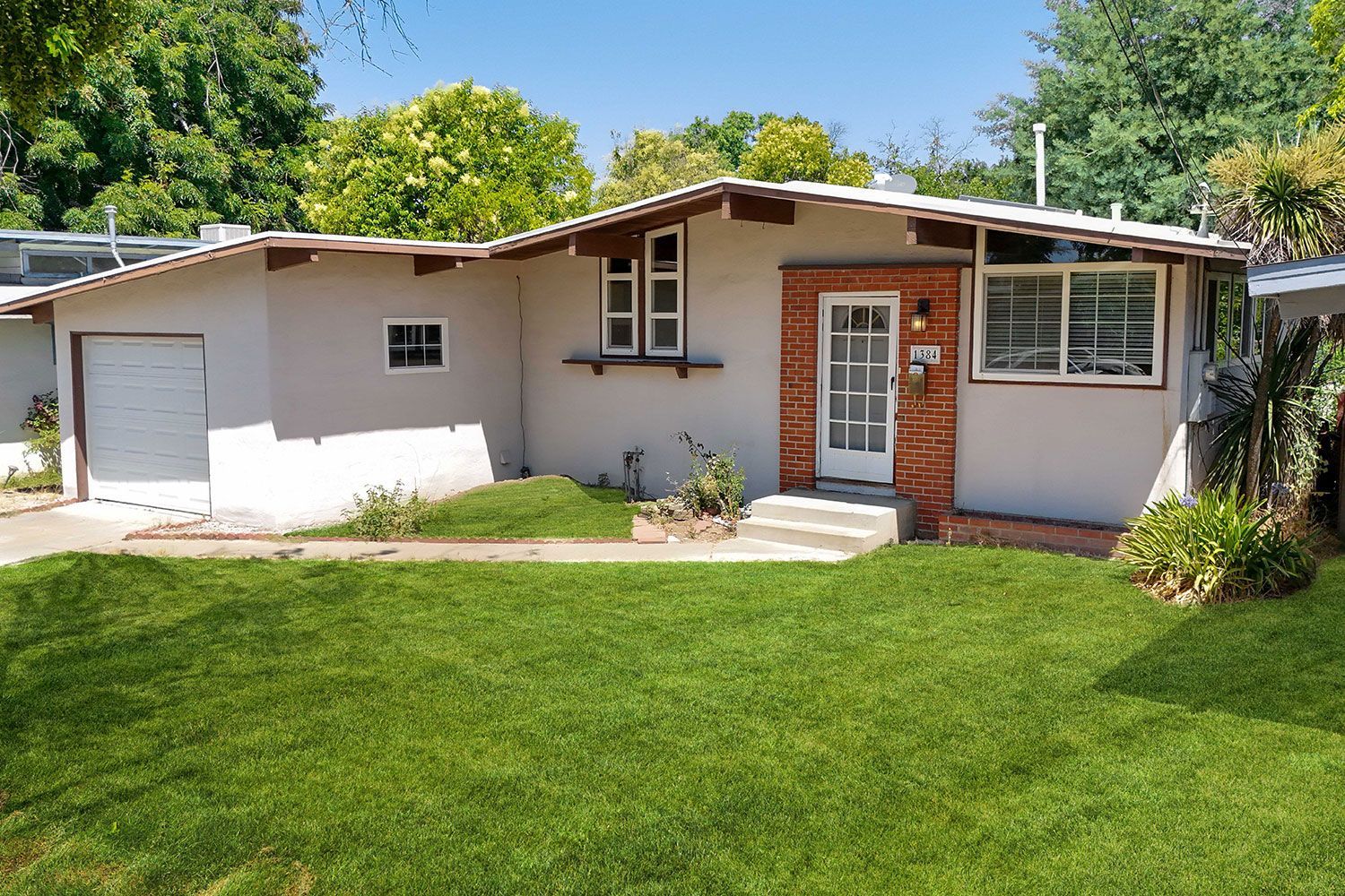 A one-story house with a garage and brick detailing. Green grass and a sunny day.