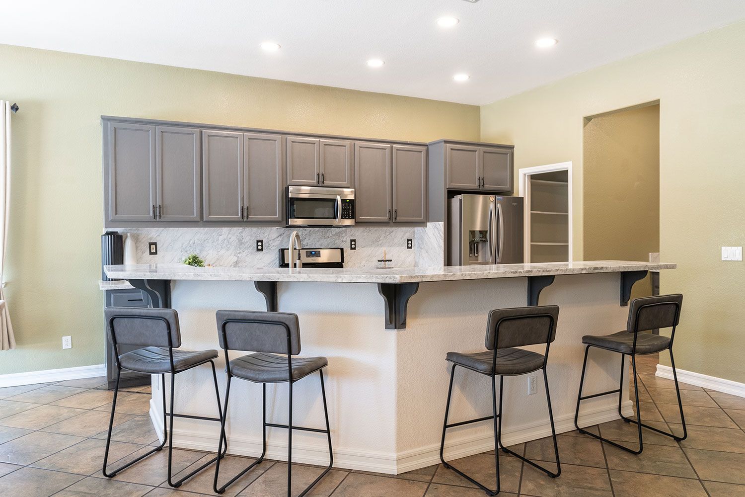 Modern kitchen with gray cabinets, marble countertops, a breakfast bar with stools, and stainless steel appliances.