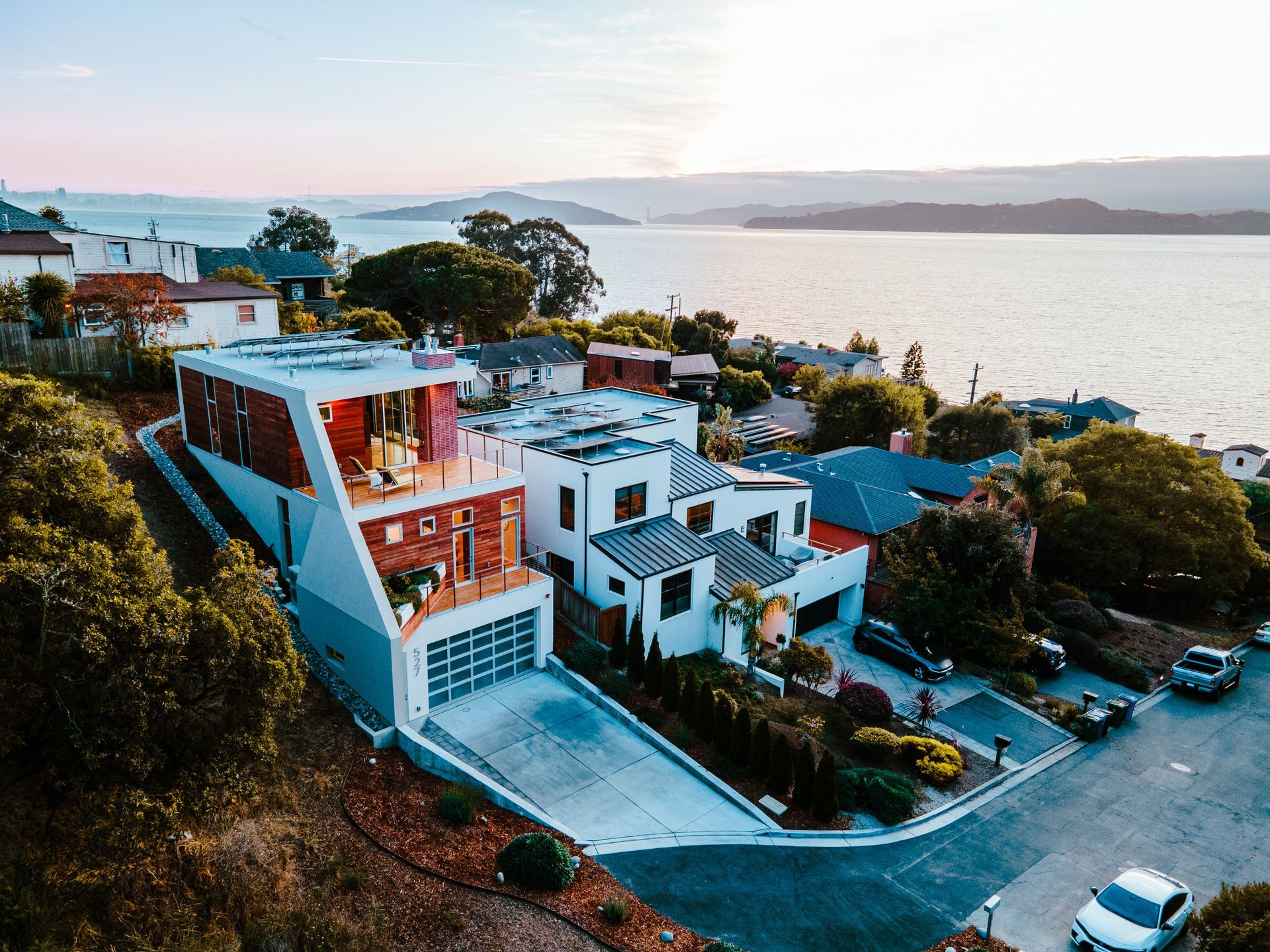 Modern houses on a hillside overlooking the water at sunset.