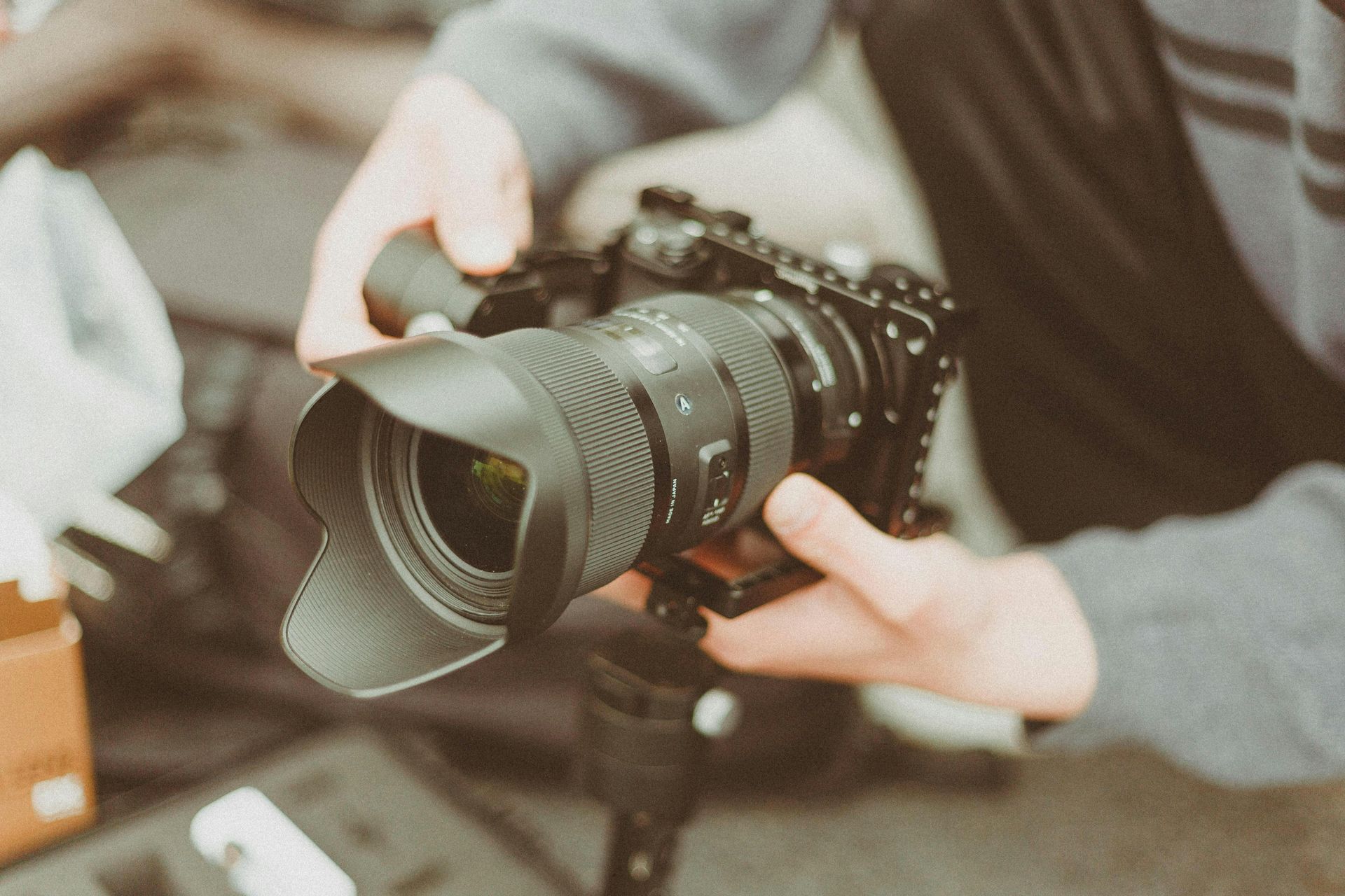 Hands holding a black camera with a large lens, set on a tripod.