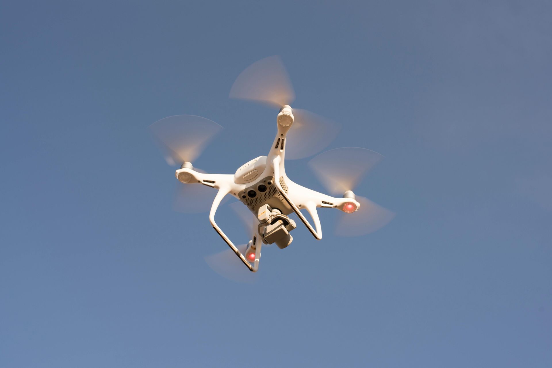 White drone with spinning propellers against a blue sky.