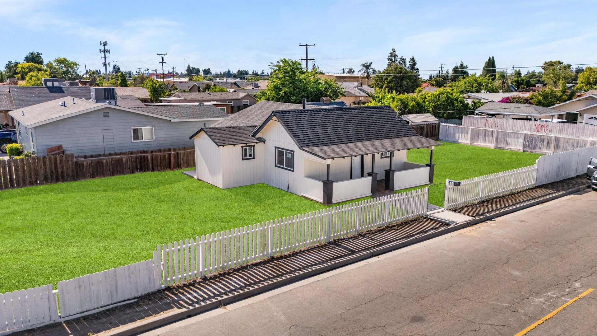 Small white house with a green lawn, white picket fence, and street view.