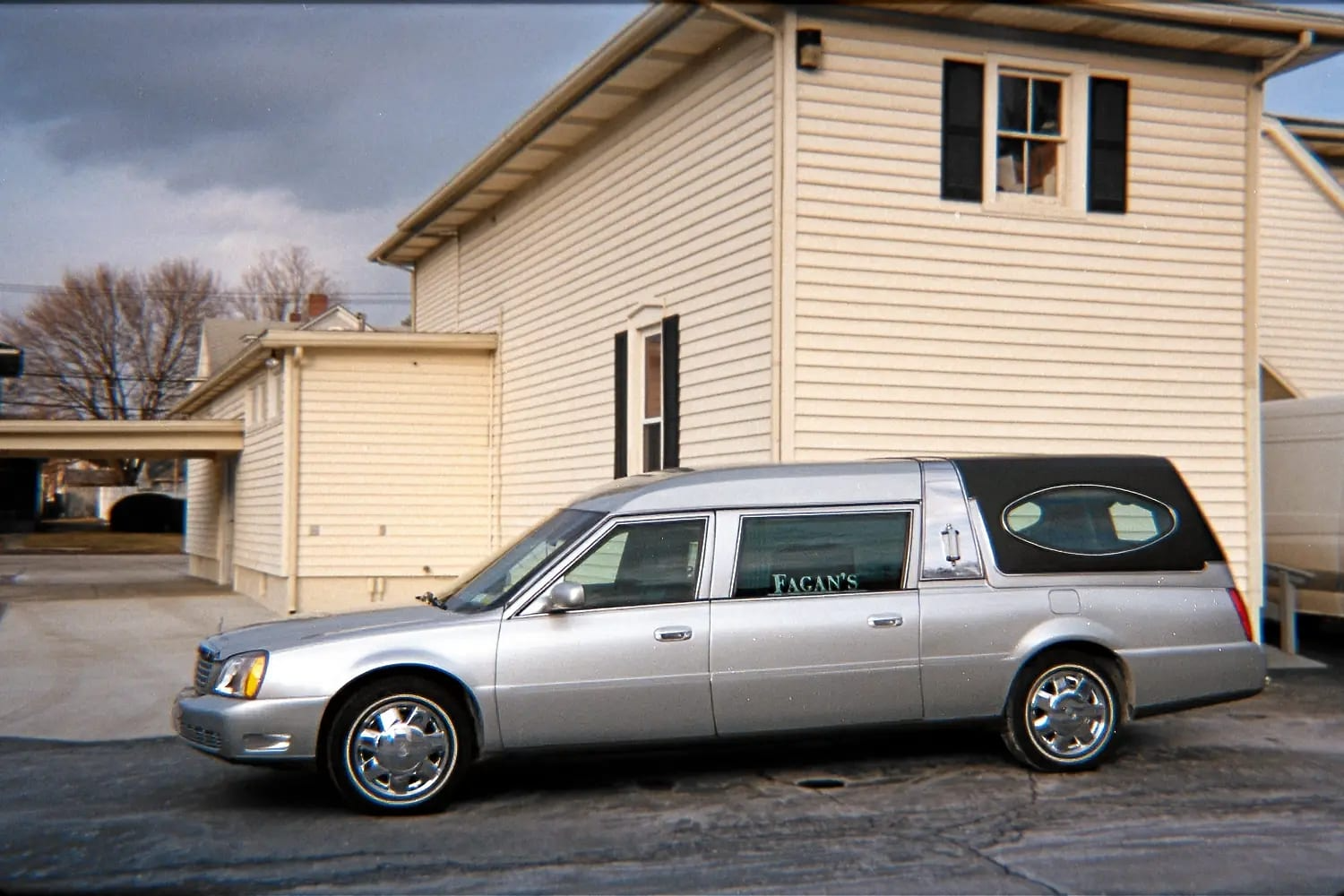 A silver funeral car is parked in front of a house