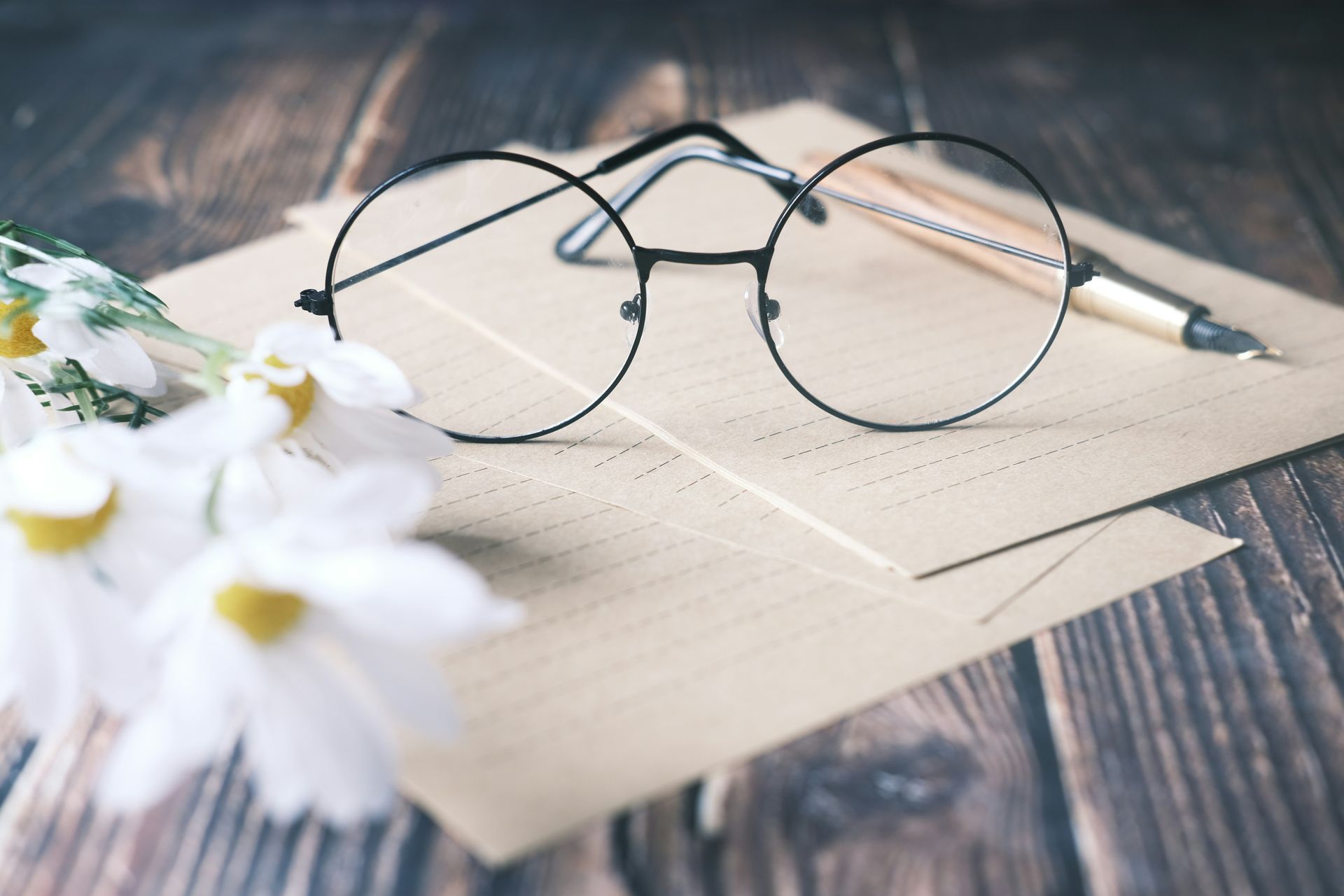 A pair of glasses sitting on top of a piece of paper next to a pen.
