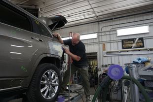 Mechanic using a tool to repair a silver car door in a garage