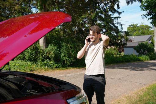 a woman is sitting on the hood of a broken down car talking on a cell phone .