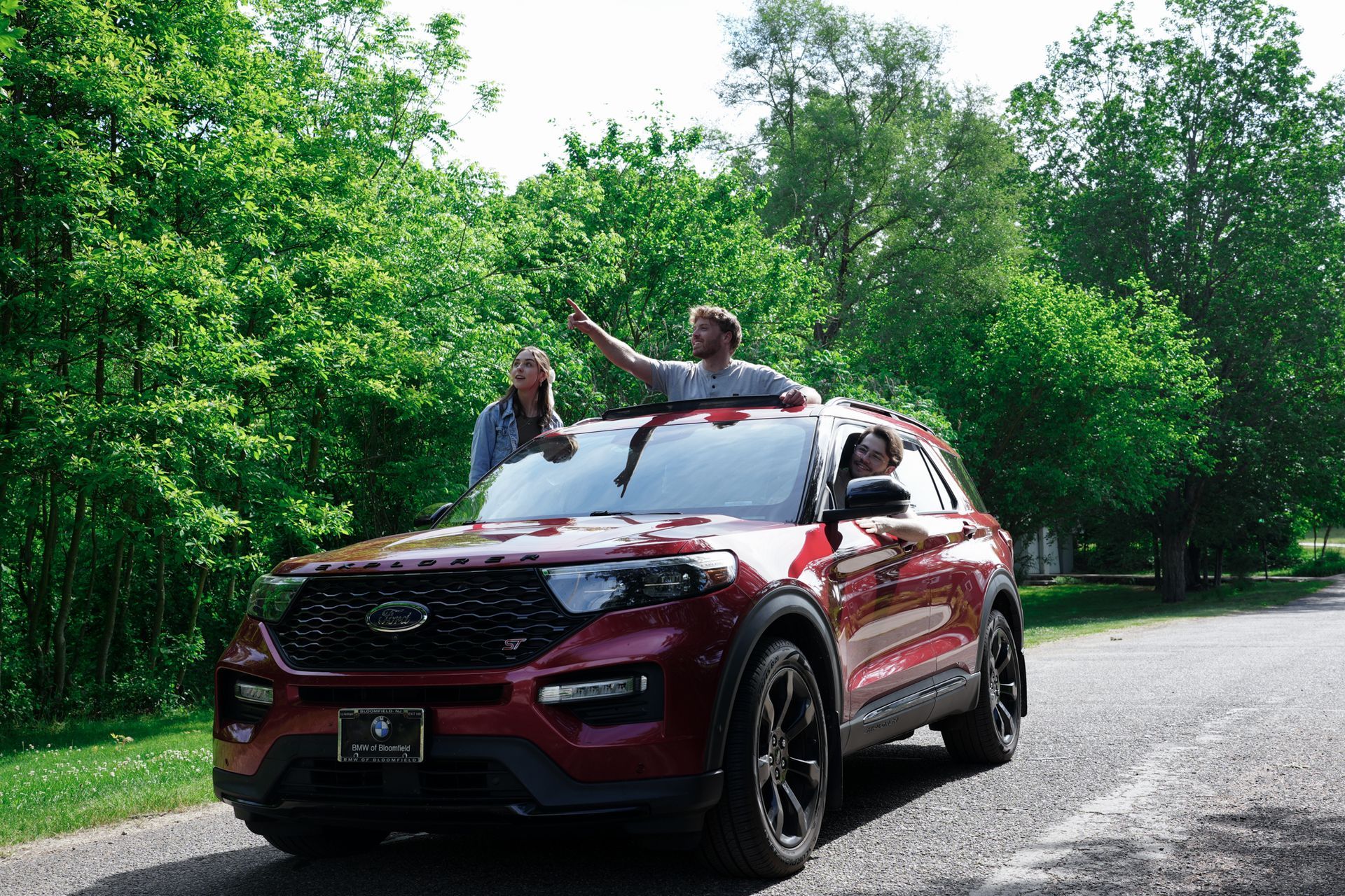 Red SUV on a forest road with two people standing through the sunroof holding arms up
