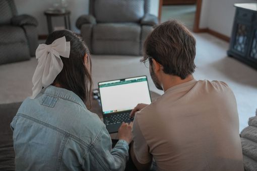 Two people sit on a couch using a laptop in a living room.
