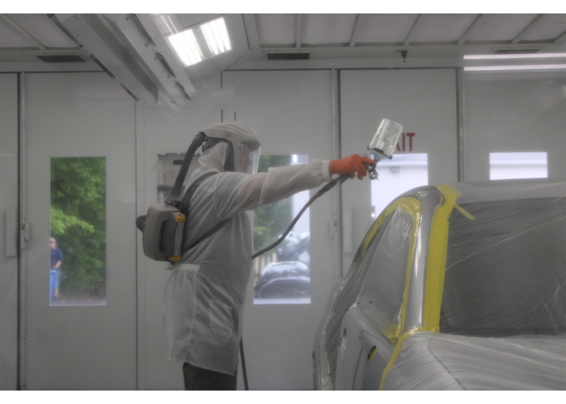 Worker applying blue vinyl wrap to a car hood in an auto shop