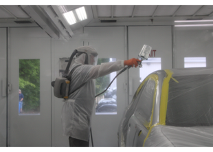 Worker applying blue vinyl wrap to a car hood in an auto shop