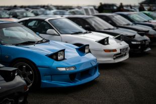 Row of parked sports cars, with a bright blue car in the foreground at a car meet.