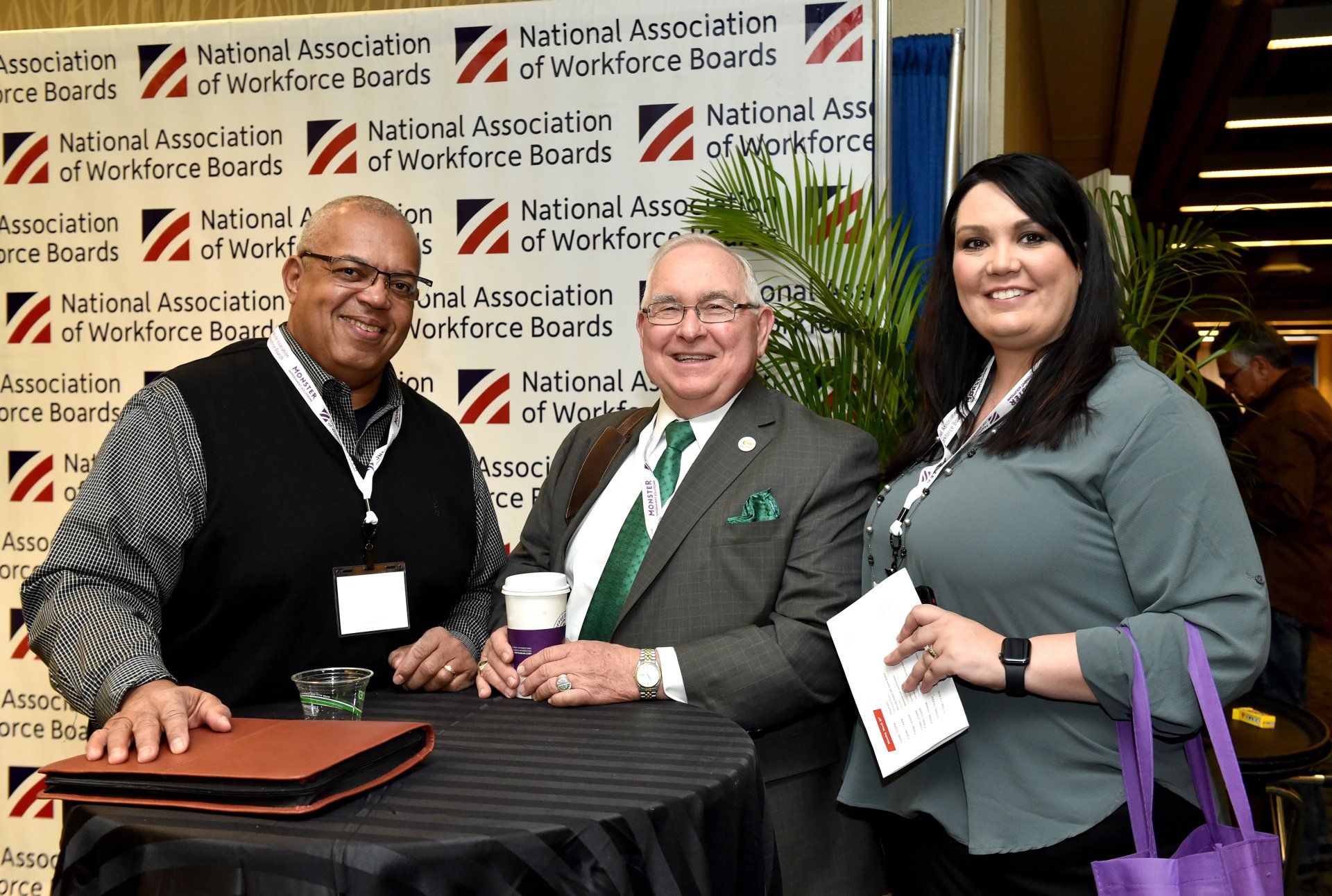 Three people are posing for a picture in front of a national association of workforce boards sign.