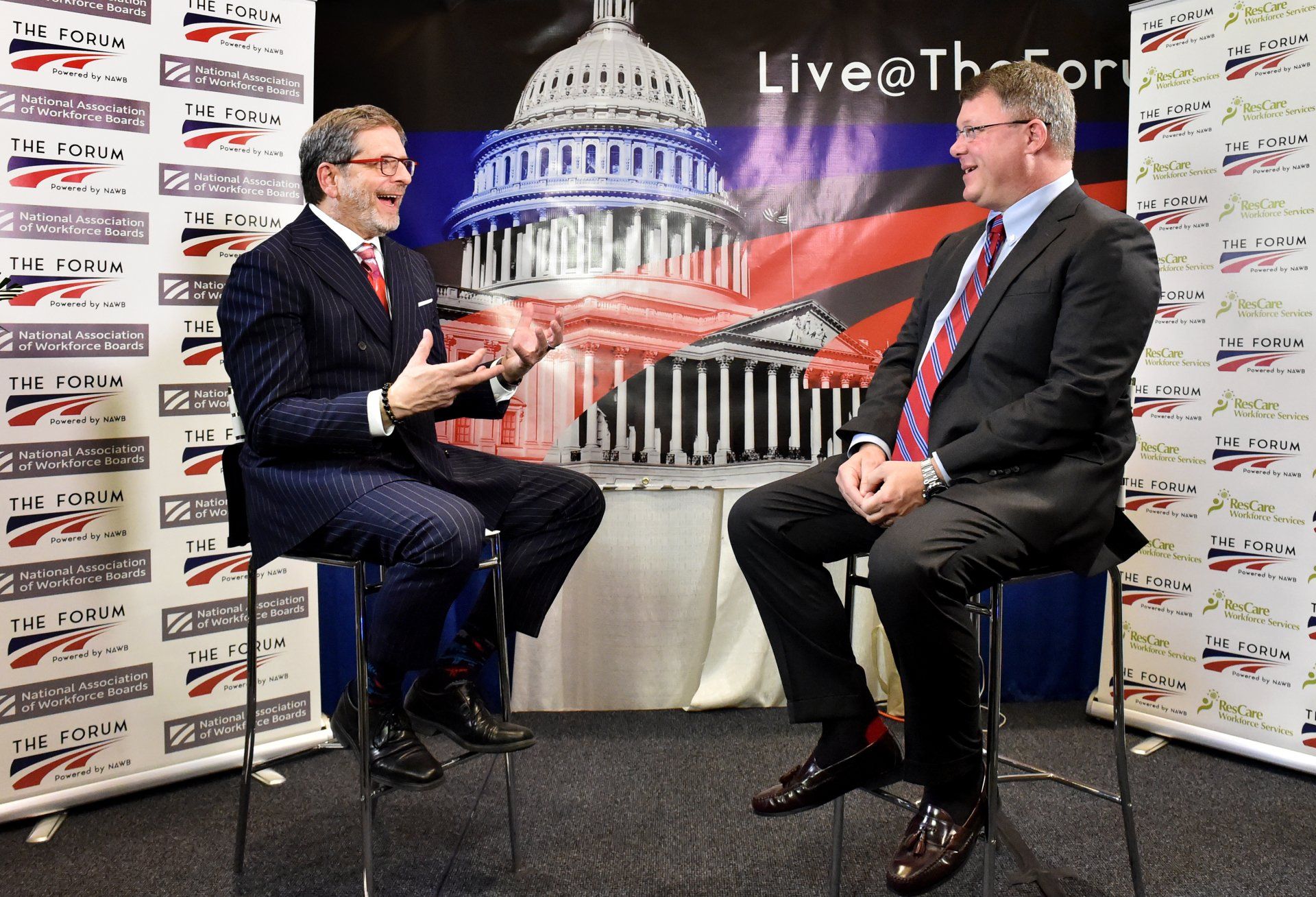 Two men are sitting in front of a capitol building and talking