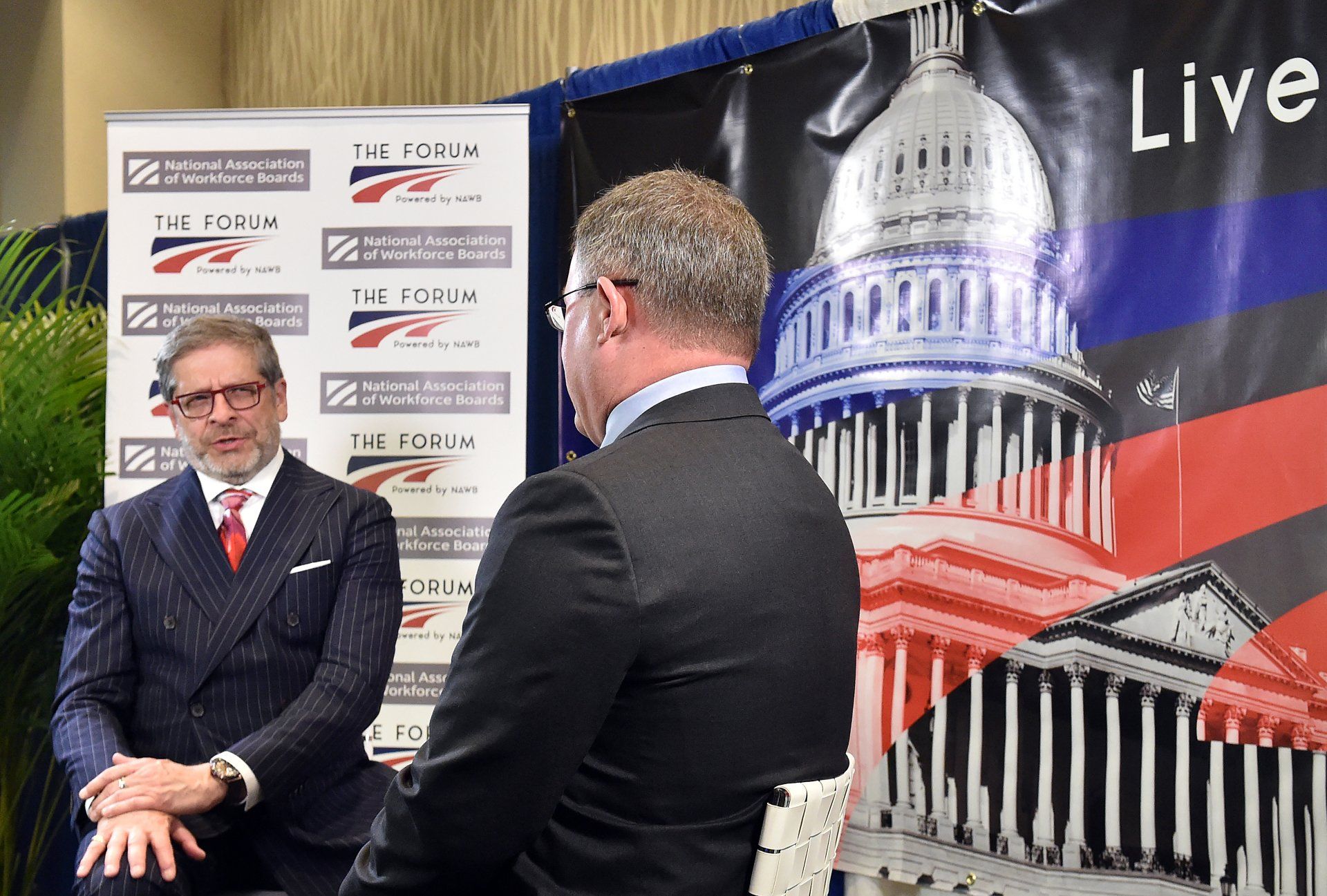 A man in a suit and tie is talking to another man in front of a capitol building.