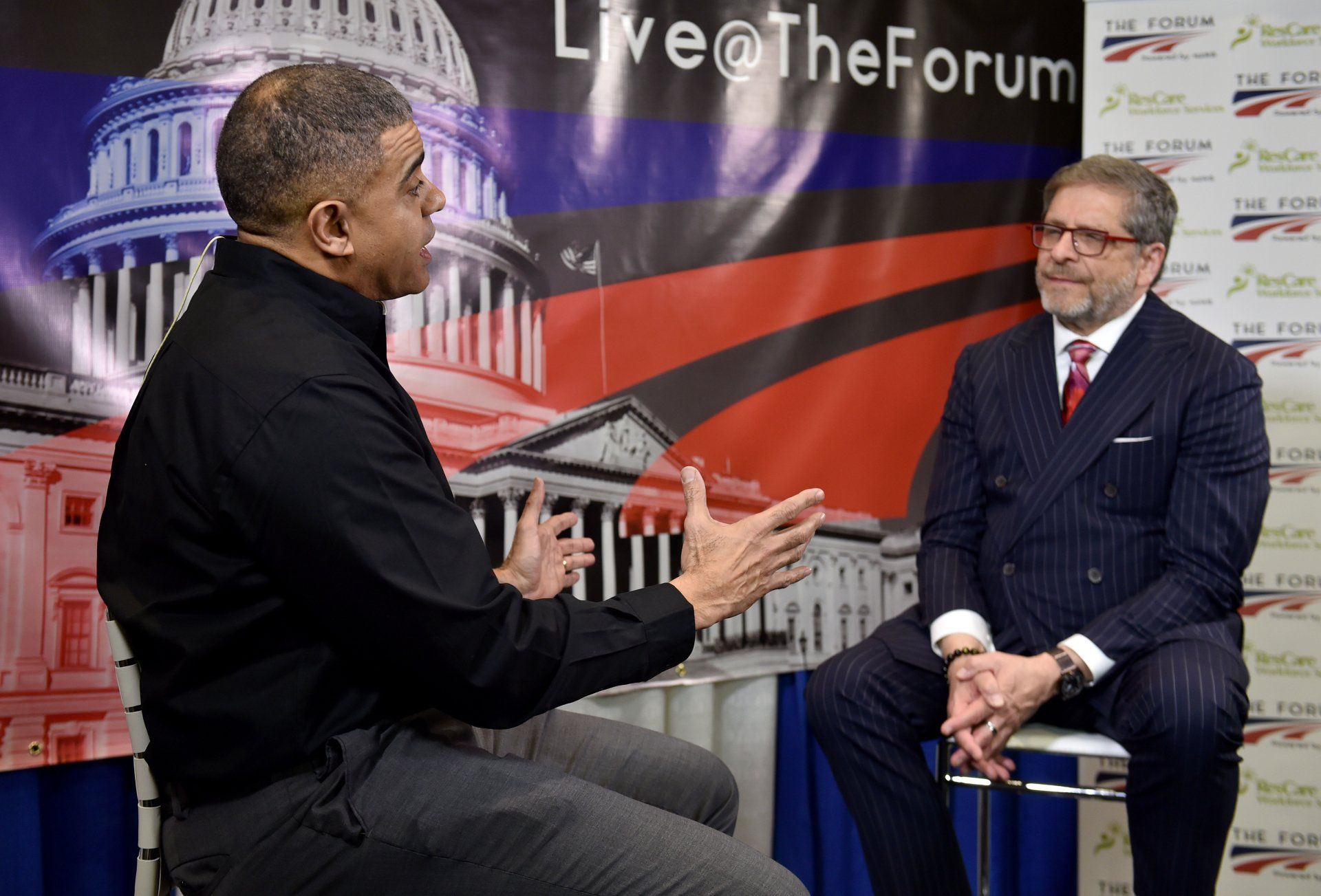 Two men are sitting in front of a sign that says live @ the forum.