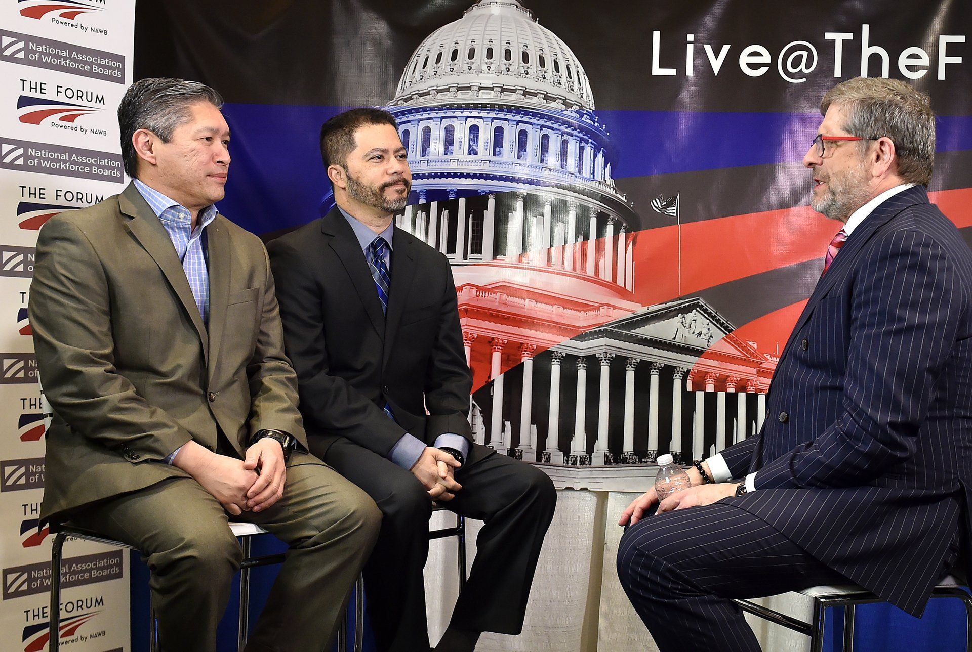 Three men in suits are sitting in front of a capitol building