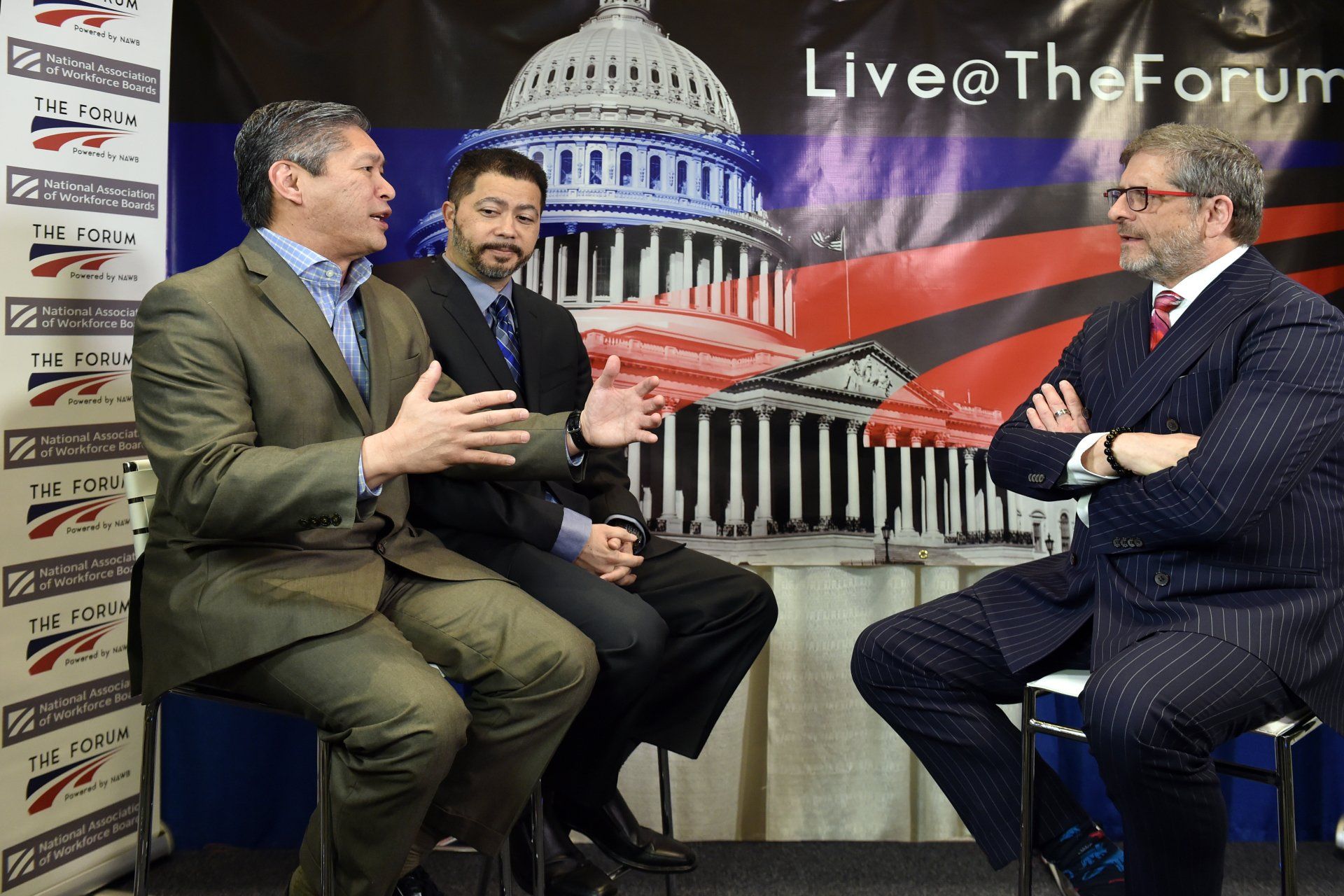 Three men are sitting in front of a live @ the forum sign