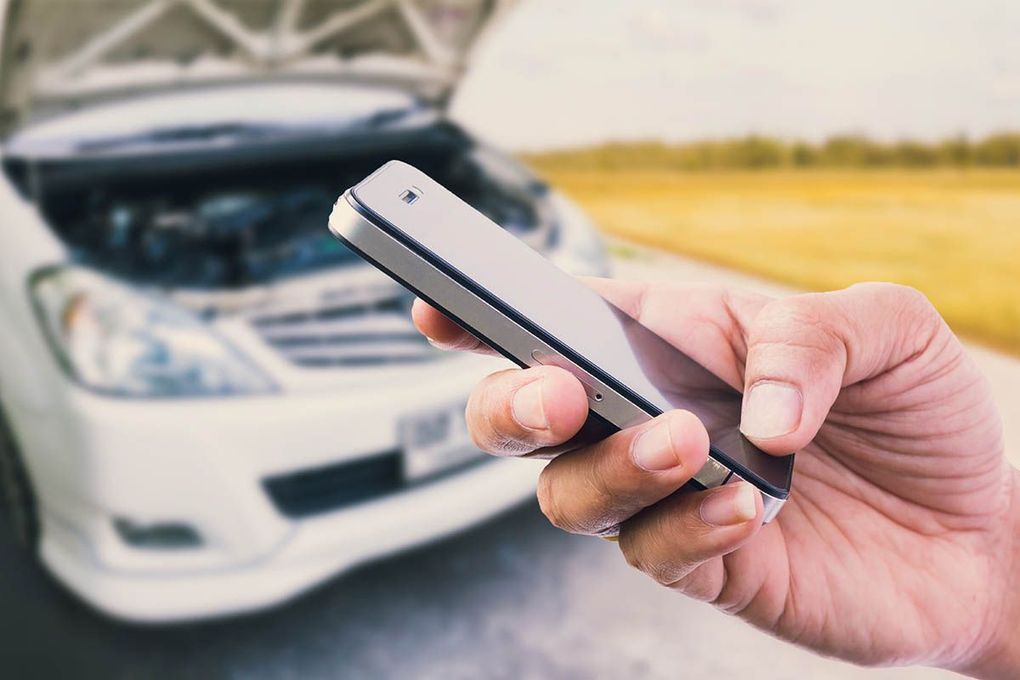 A person is holding a cell phone in front of a broken down car.