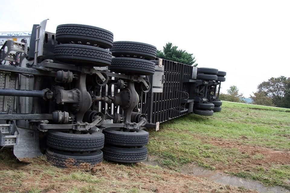 A semi truck is turned over on its side in a grassy field.