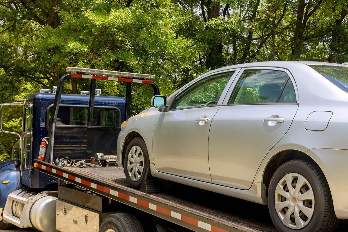 A silver car is being towed by a tow truck.