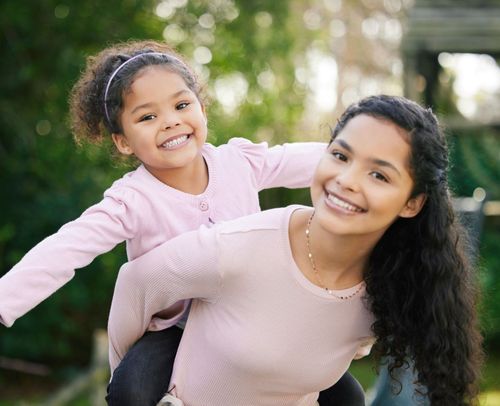 A woman is carrying a little girl on her back.