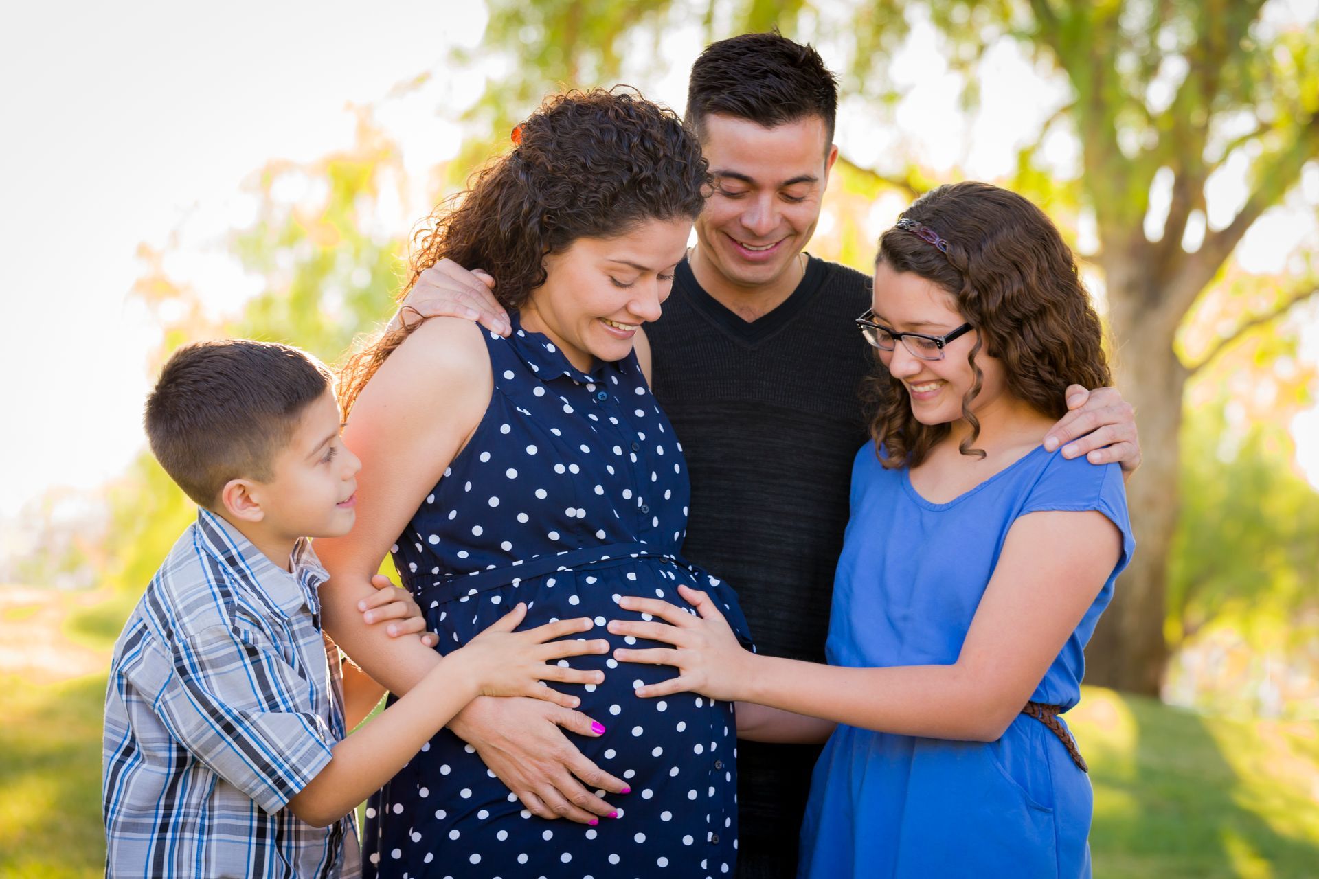 A family is standing around a pregnant woman 's belly.