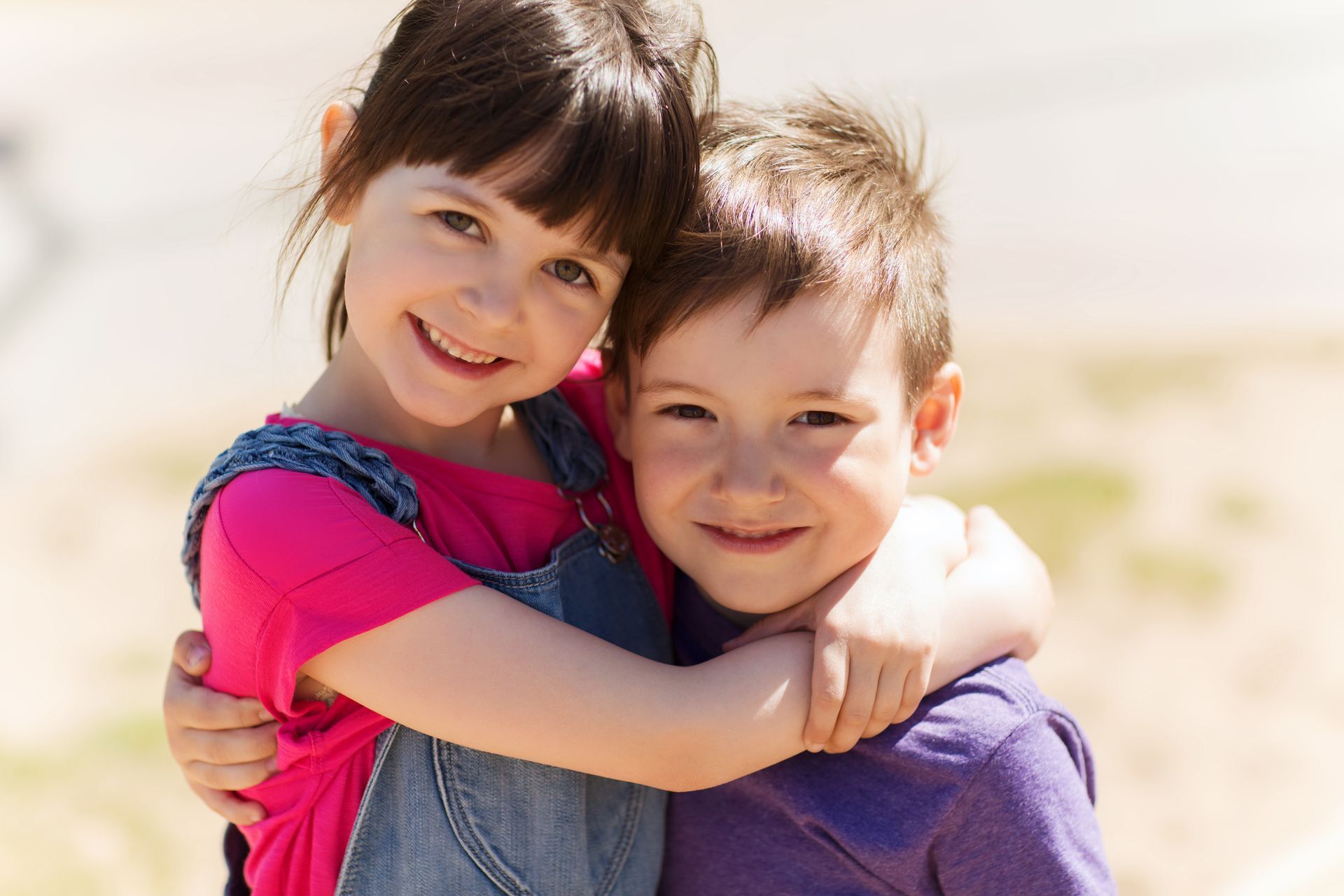 A boy and a girl are hugging each other and smiling for the camera.