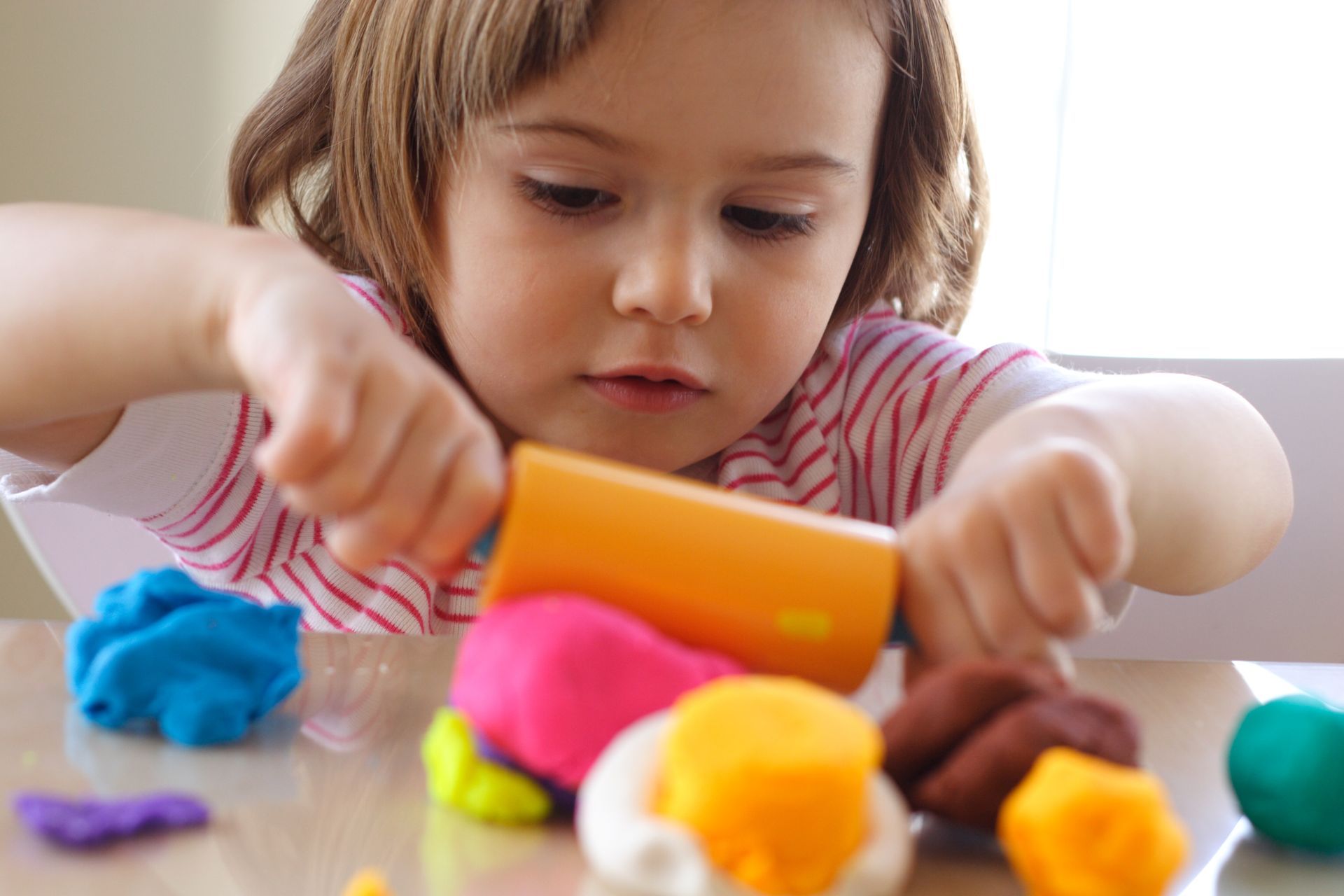 A little girl is playing with play dough at a table.