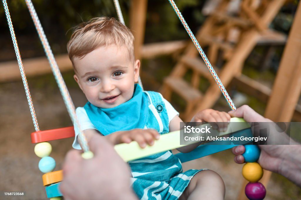 A little boy is sitting on a wooden swing.